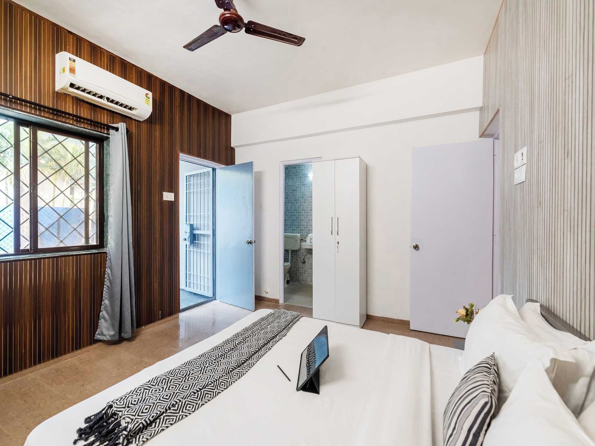 Un dormitorio con cama, armario, ventilador de techo y baño visible a través de una puerta abierta.