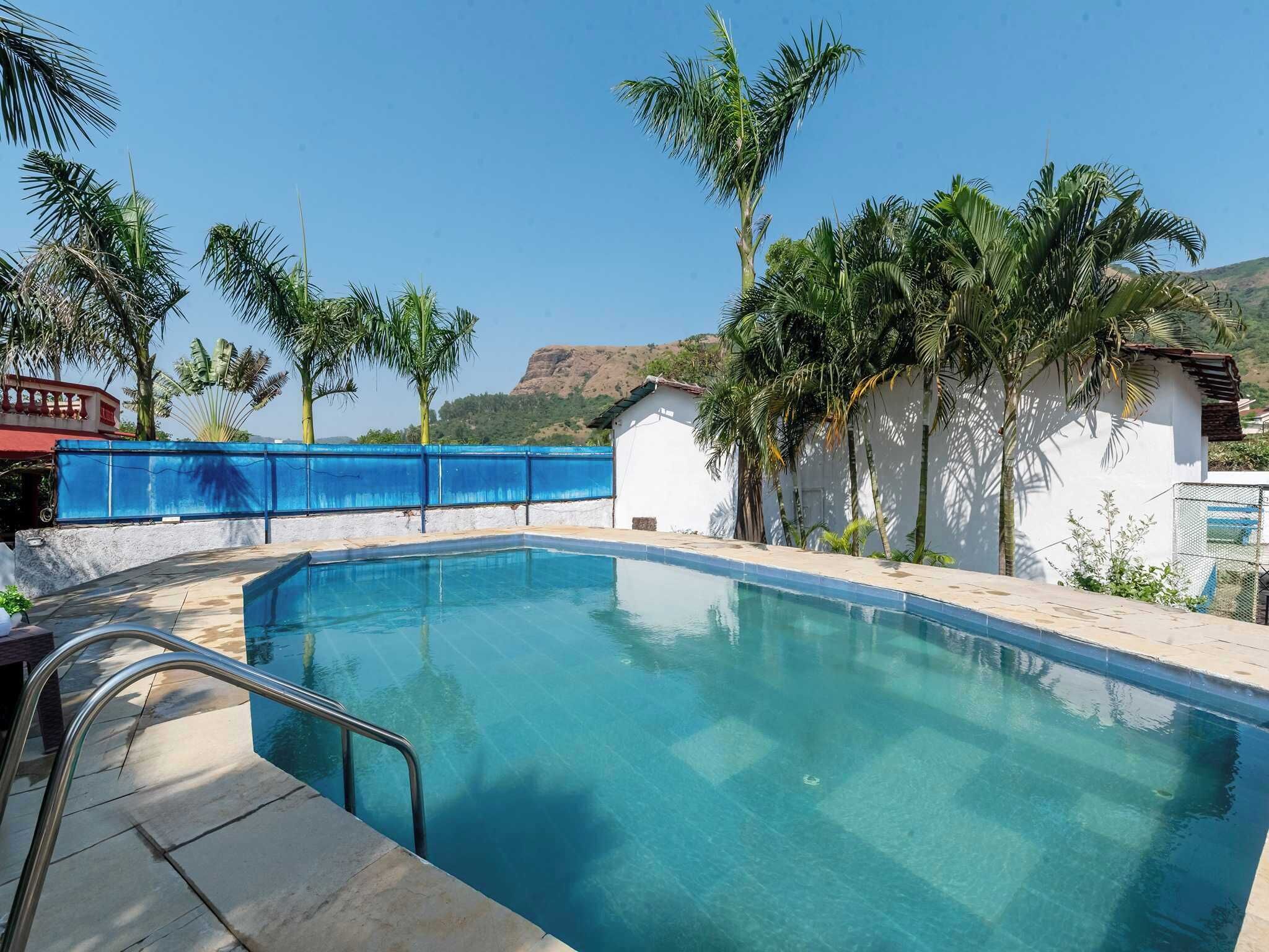 A swimming pool with a clear blue water, surrounded by palm trees and a white building with a red roof.