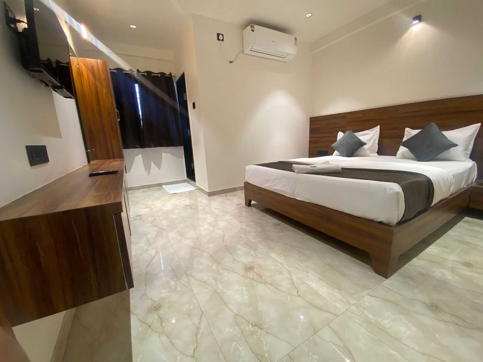 Habitación de hotel con cama, escritorio de madera, espejo y aire acondicionado.