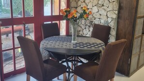 Un comedor con una mesa redonda, cuatro sillas, un jarrón con flores y una pared de piedra.
