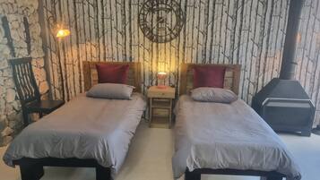 A room with two beds, a wall clock, a table lamp, and a fireplace.