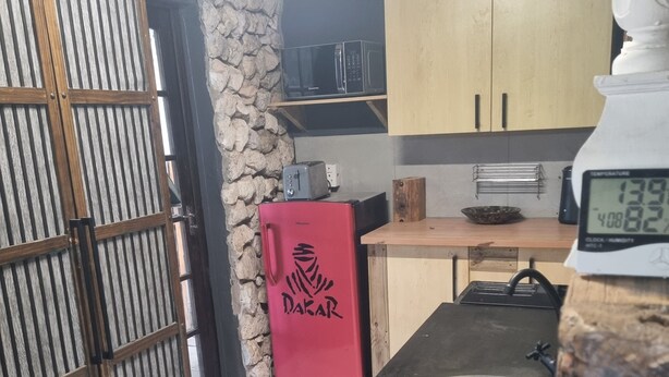 Una cocina con estufa a gas, un refrigerador rojo y una pared de piedra.