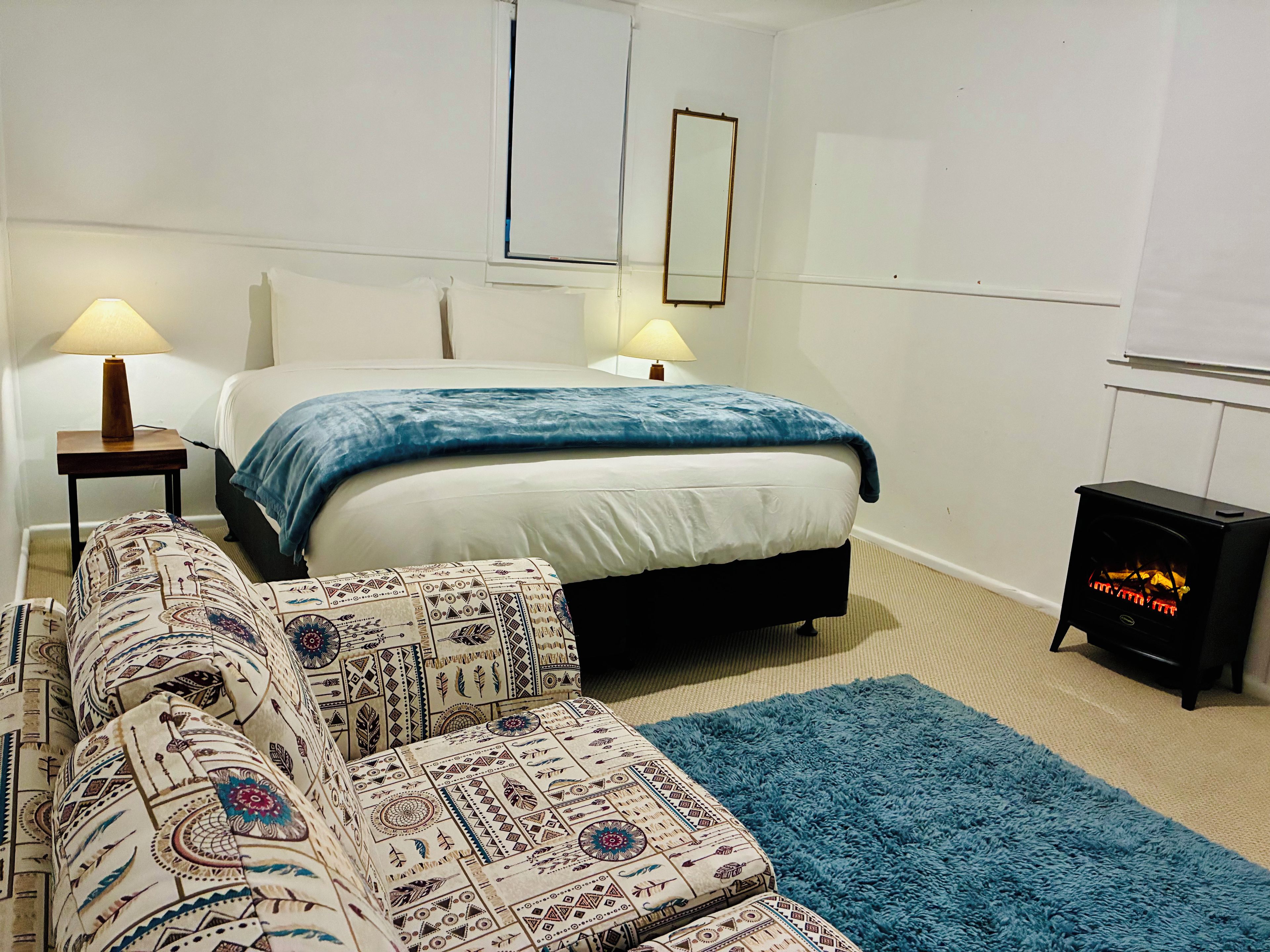 Een slaapkamer met een bed, twee bedlampen, een gestreept sofa en een kleine, zwarte verwarming.