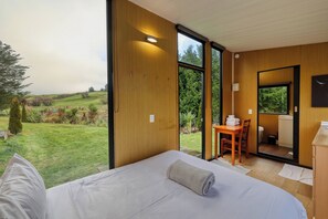 A bedroom with a large window, a bed, a desk, and a bathroom. - The Black Barn At Puketitiri (Puketitiri)