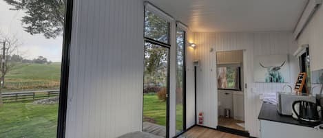 A modern bedroom with a large window, a small bathroom, and a view of the countryside.
