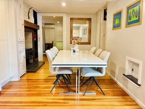 A dining area with a white table and chairs, a mirror on the wall, and a wooden floor. - The Black Barn At Puketitiri (Puketitiri)