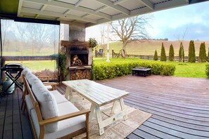 An outdoor patio with a stone fireplace, a sofa, and a table. - The Black Barn At Puketitiri (Puketitiri)