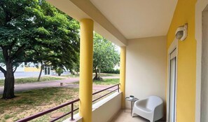A balcony with yellow walls, a white chair, and a small table with a plant. - MyStay - Moura Lighthouse (Vilamoura)