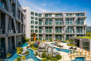 A modern hotel with multiple floors, a rooftop pool area, and a landscaped pool with rock formations. - UTL B131 Resort Duplex 5 Pools (Tambon Rawai)