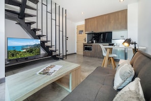 Una sala de estar moderna con un sofá, una mesa de centro, un televisor, una escalera y una zona de cocina.