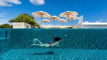 Una piscina con agua cristalina, una persona nadando y varias sombrillas.
