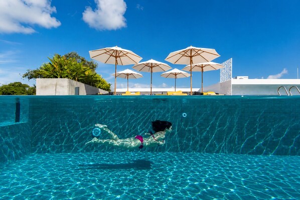 Una piscina con agua cristalina, una persona nadando y varias sombrillas.