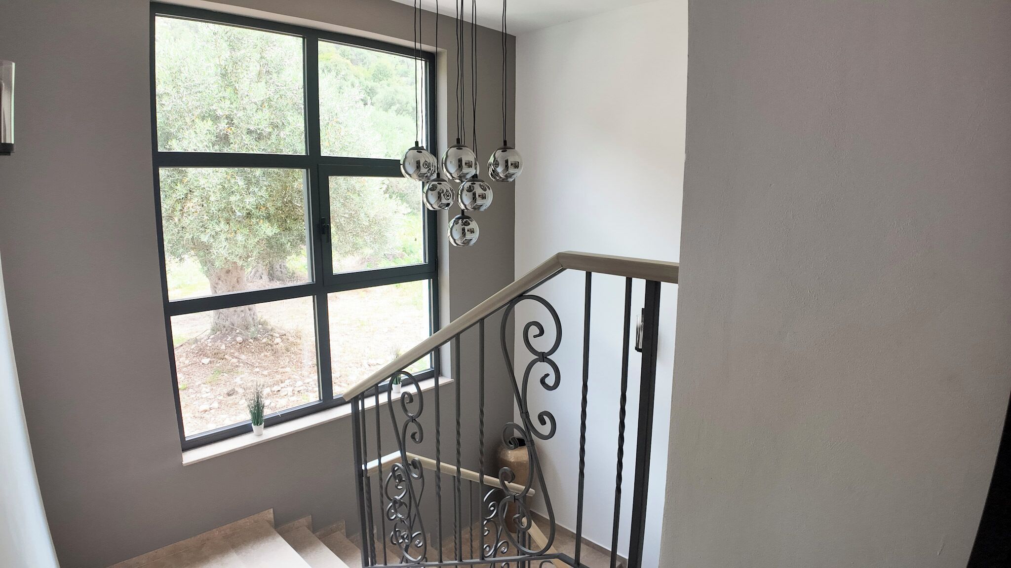 A staircase with a wrought iron railing and a large window with a view of greenery.