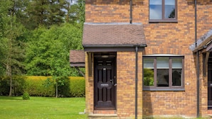 A two-story brick house with a black front door, a satellite dish, and a window. - Modern Home in Gleneagles Village | 2 Bed (Auchterarder)