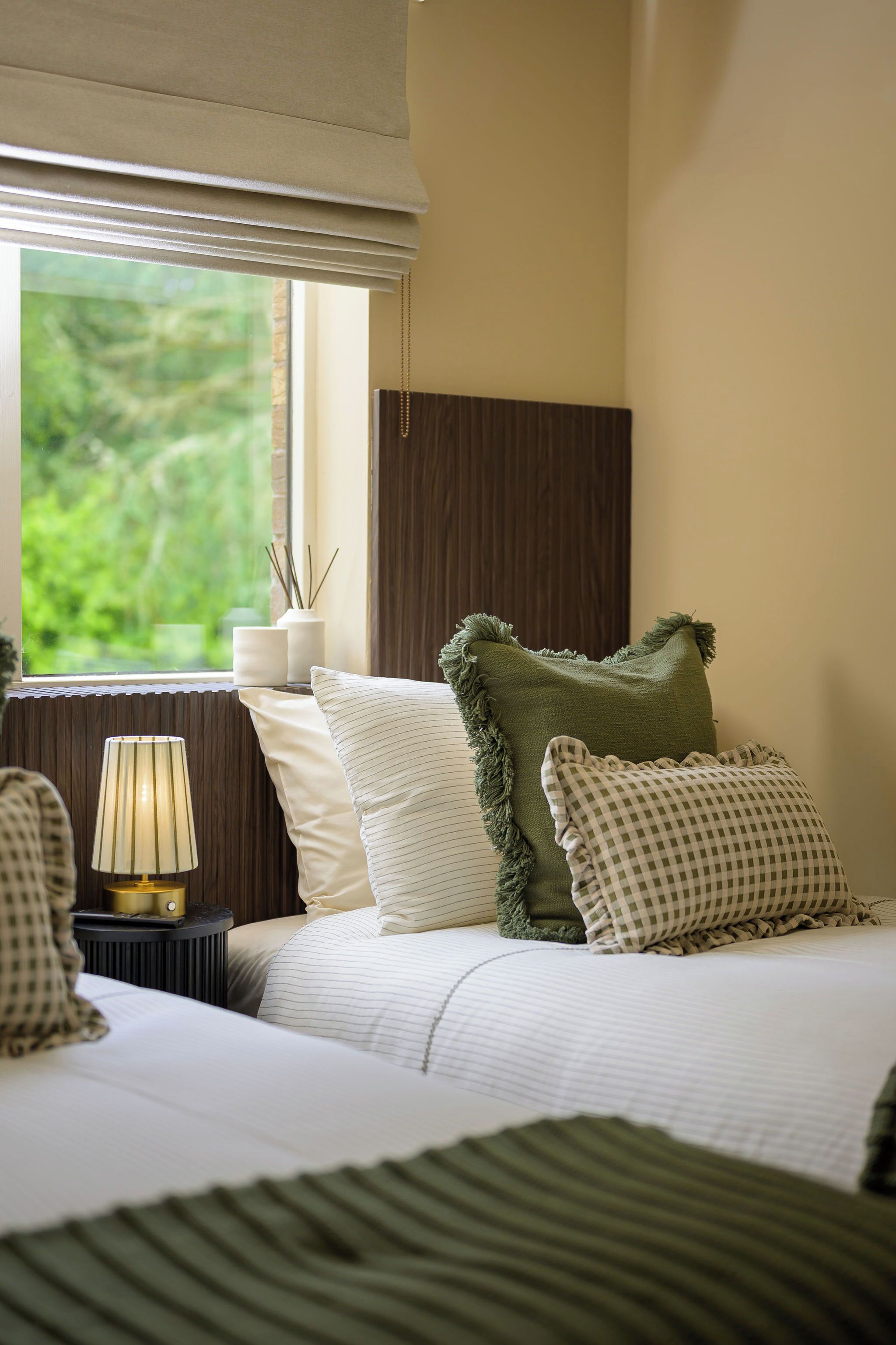 Une chambre bien rangée, avec un lit, une lampe de chevet et une fenêtre donnant sur un paysage verdoyant.
