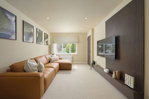 A modern living room with a sectional sofa, a flat-screen TV mounted on a wall, and framed artwork on the wall.