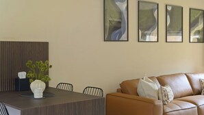 A modern living room with a brown leather sofa, a dining table with chairs, and three abstract paintings on the wall. - Modern Home in Gleneagles Village | 2 Bed (Auchterarder)