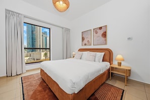 A hotel room with a large bed, two bedside lamps, a view of tall buildings, and two framed artworks on the wall. - Bloomfields 3br in Rimal 4 JBR (Dubai)