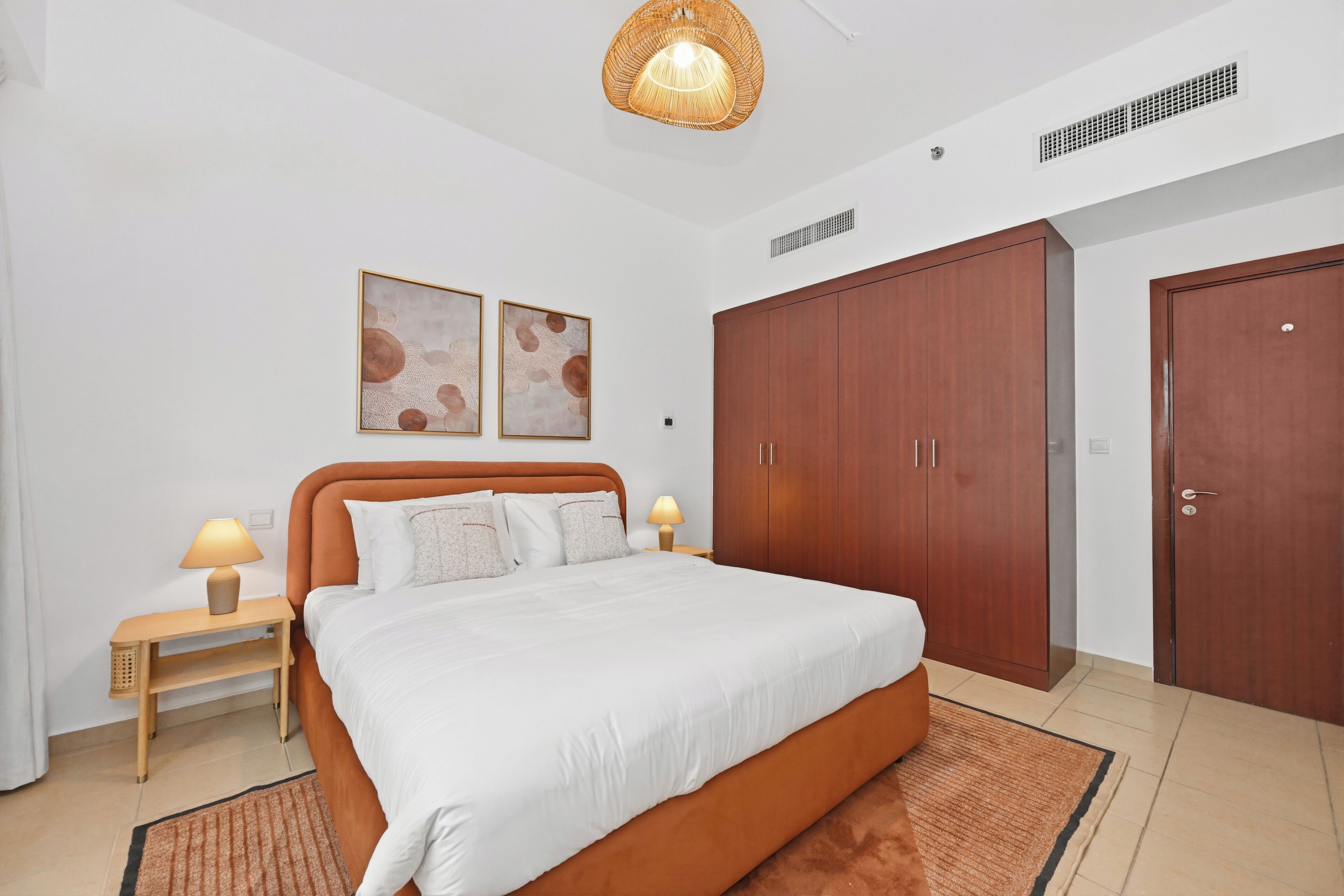 A bedroom with a bed, nightstands, a wooden wardrobe, and two wall art pieces.