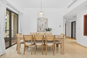 A dining area with a round table, six chairs, a hanging light fixture, and a potted plant. - Bloomfields 3br in Rimal 4 JBR (Dubai)