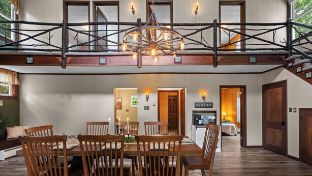 A dining area with a wooden table and chairs, a chandelier, and a staircase with a wooden railing. - Lakefront Retreat,Sleeps 8, Kayaks & Fishing (Pine Grove)