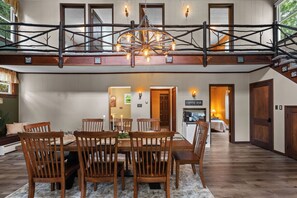 A dining area with a wooden table and chairs, a chandelier, and a staircase with a wooden railing.