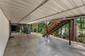 A covered outdoor area with a concrete floor, a wooden staircase, and a view of trees and a water body. - Lakefront Retreat,Sleeps 8, Kayaks & Fishing (Pine Grove)