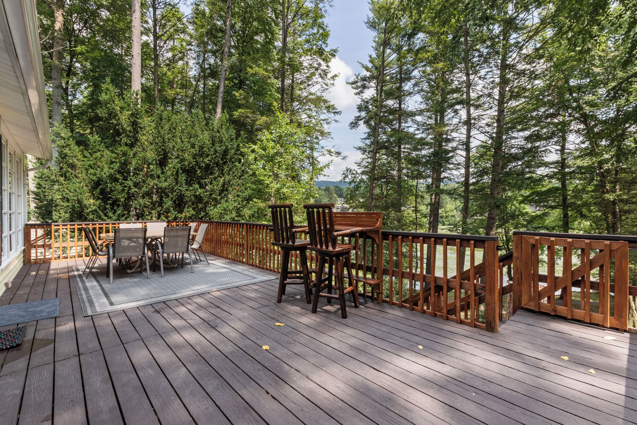 Une terrasse en bois, agrémentée d’une table et de chaises, entourée d’une balustrade en bois, et offrant une vue sur une zone boisée.