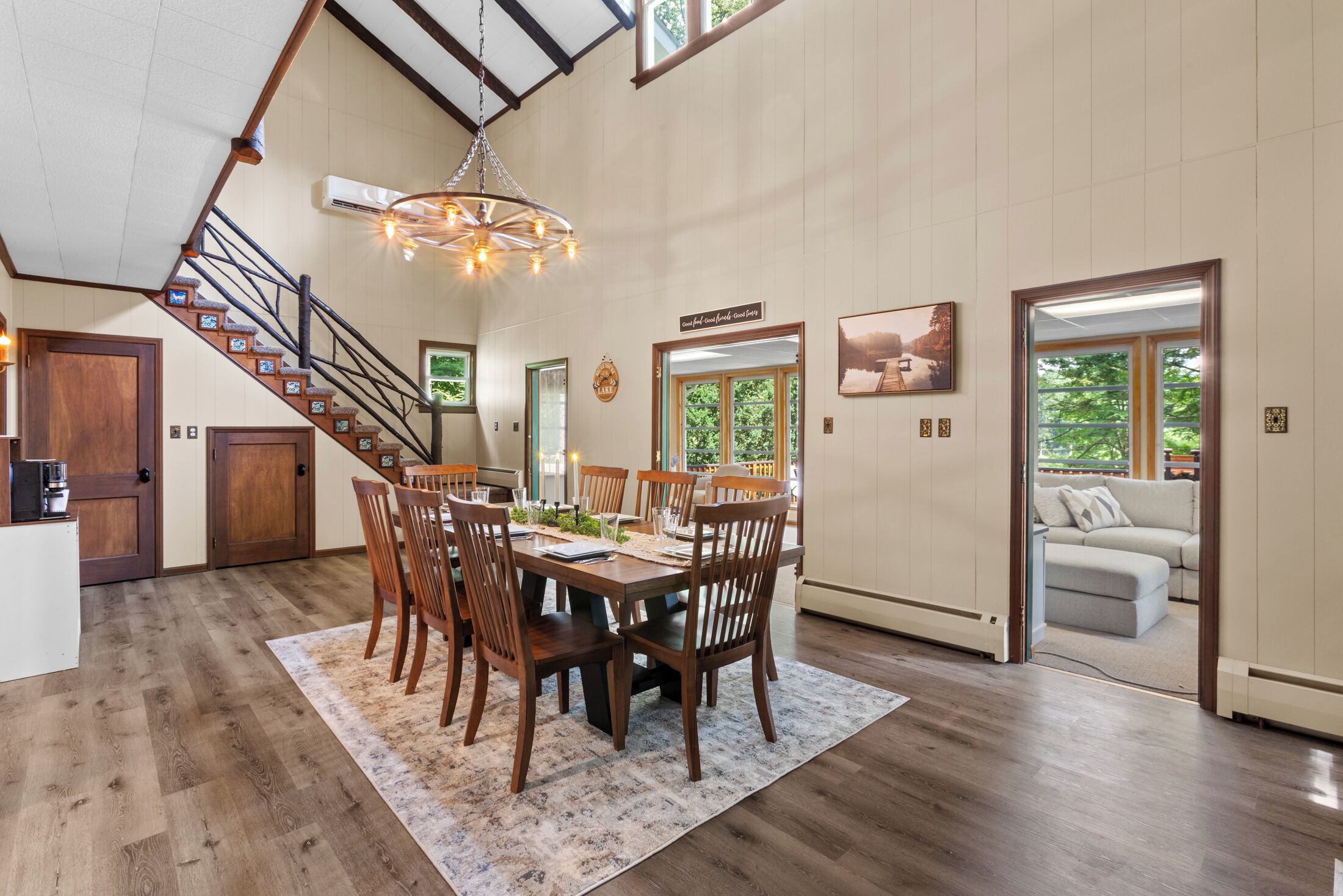 A spacious dining area with a high ceiling, wooden staircase, and a view of the outdoors.