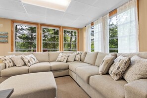A beige sectional sofa with patterned cushions, a small table, and a window with a view of trees.