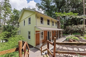 A two-story house with a porch, surrounded by a garden and trees. - Lakefront Retreat,Sleeps 8, Kayaks & Fishing (Pine Grove)