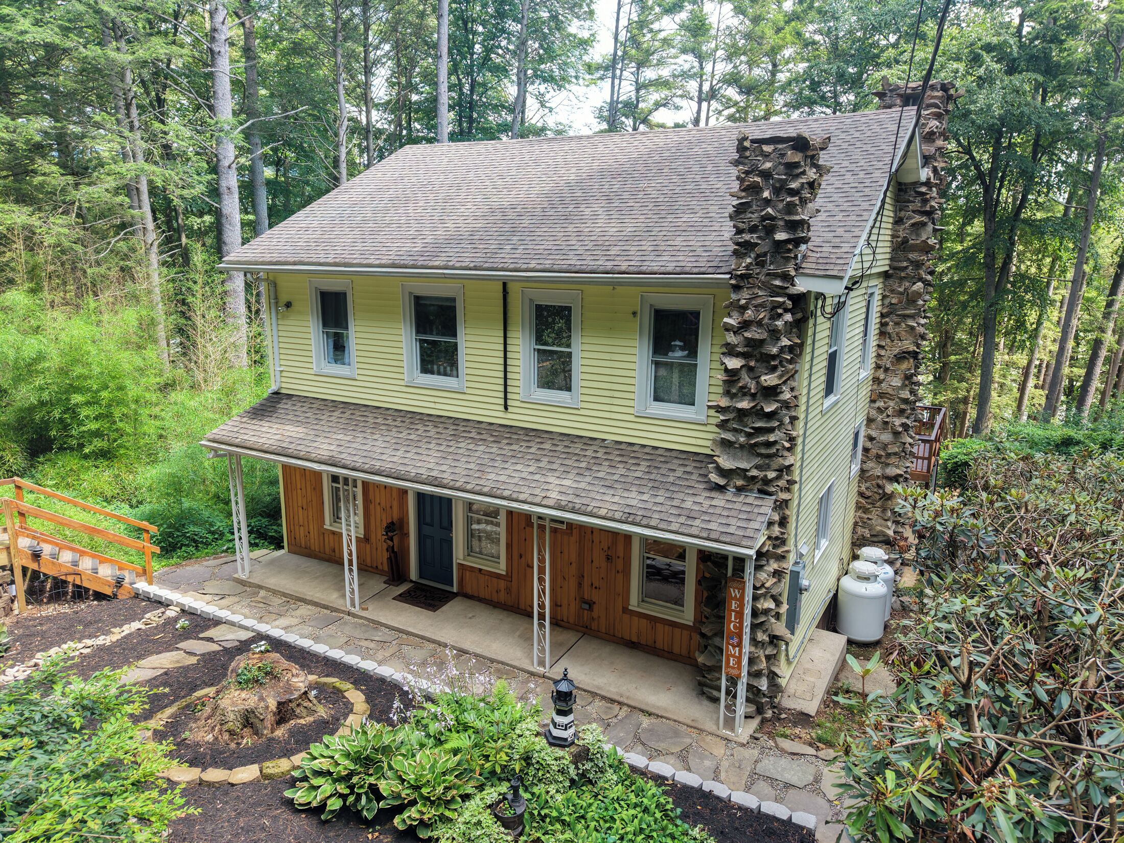 A two-story house with a porch, surrounded by a forested area.