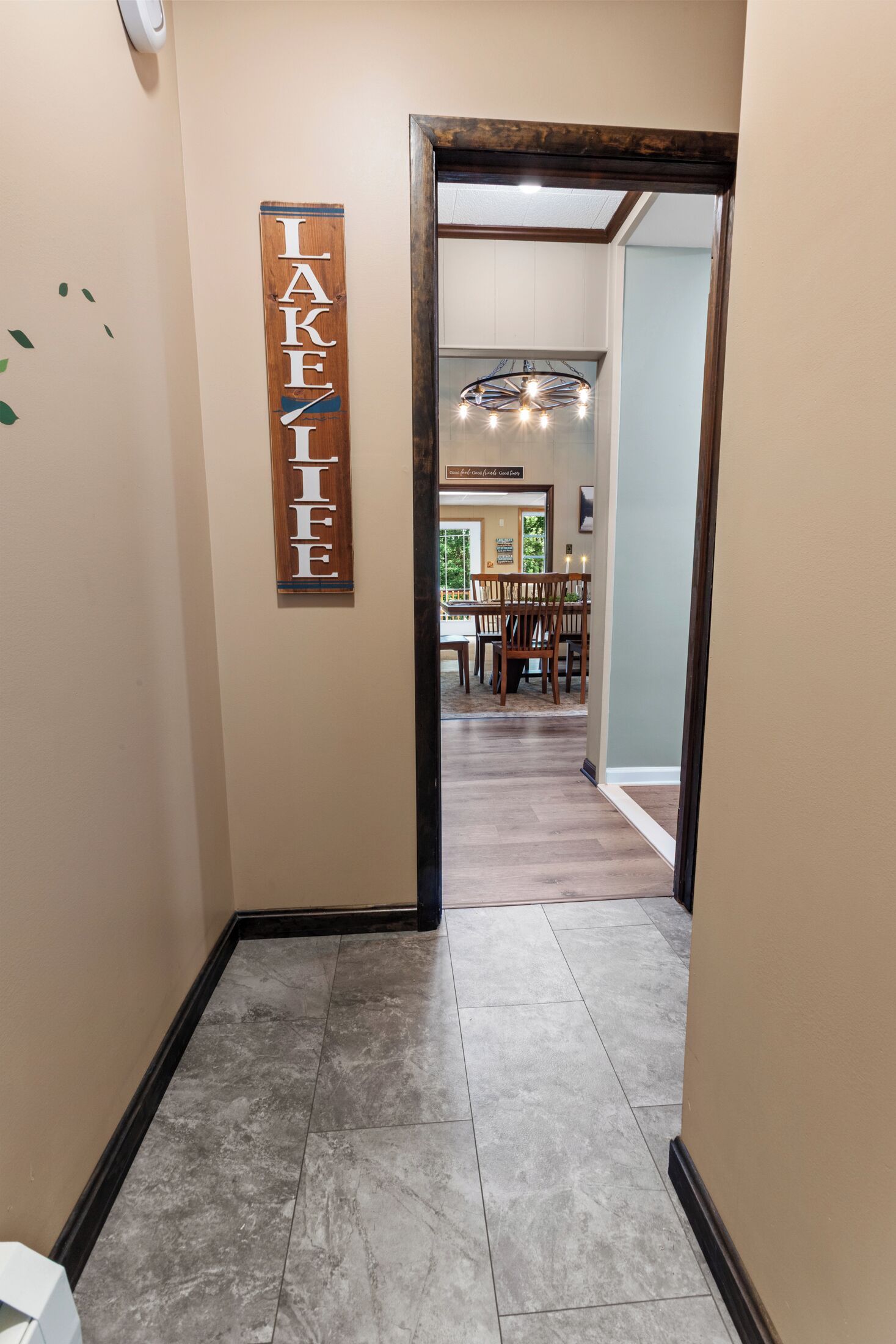 A hallway with a wooden sign reading 'LAKEFIELF' on the wall, leading to a dining area with a chandelier and wooden furniture.