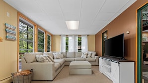 A modern living room with a sectional sofa, a flat-screen TV, and large windows. - Lakefront Retreat,Sleeps 8, Kayaks & Fishing (Pine Grove)