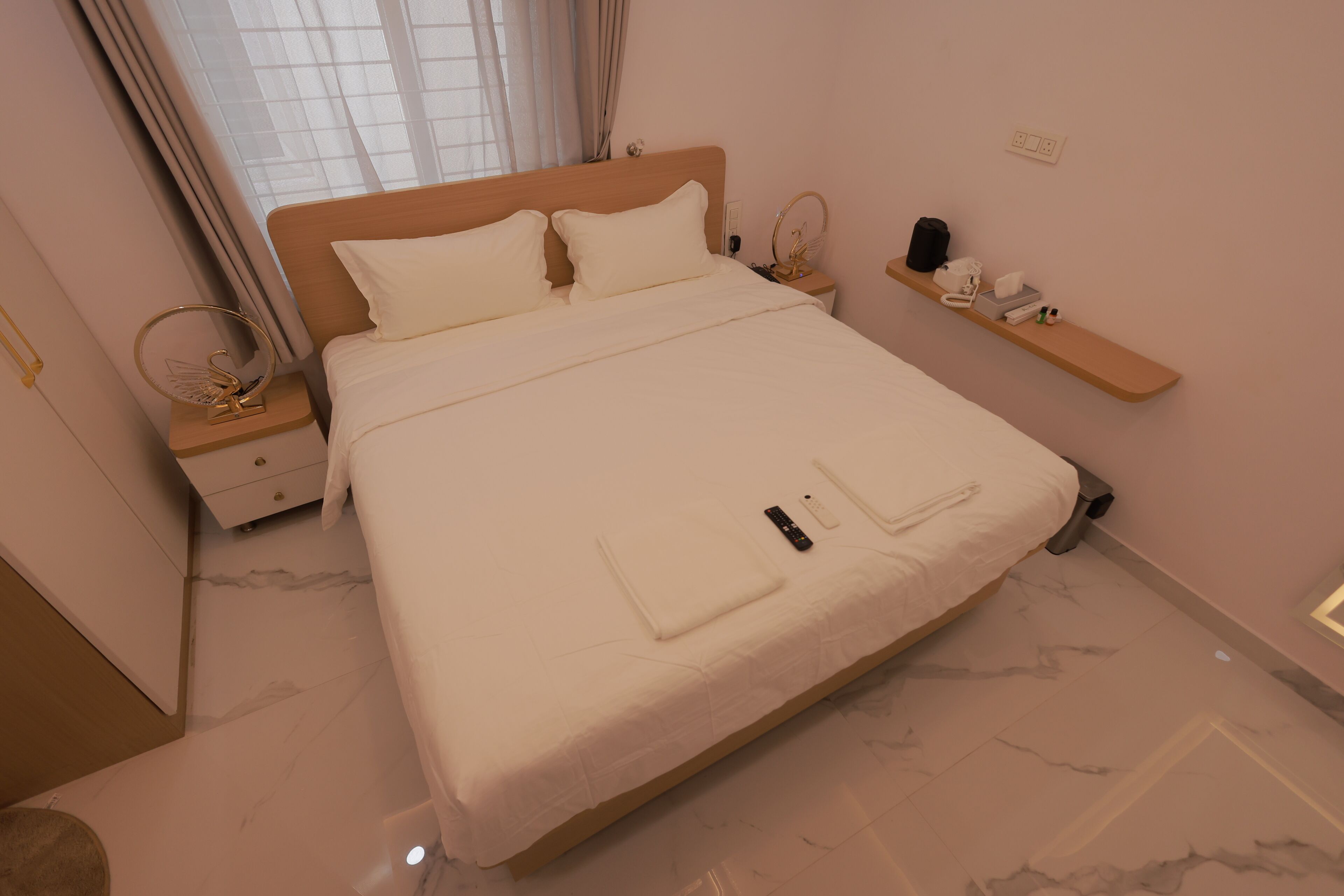 Una cama bien hecha con almohadas, una mesita de noche con lámpara y un estante con artículos de tocador.