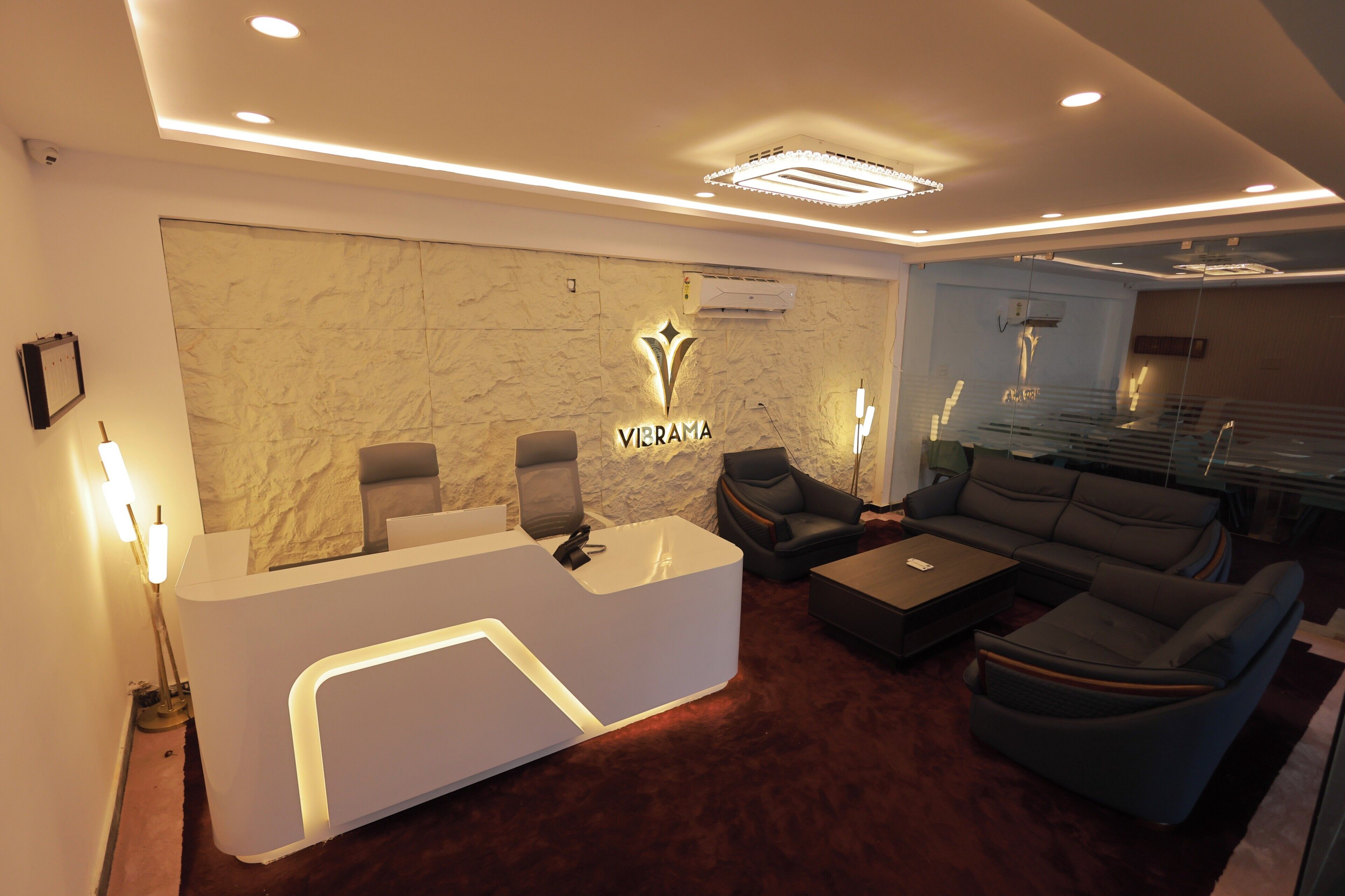 A reception area with a marble wall, a reception desk, two armchairs, a sofa, and a glass partition.