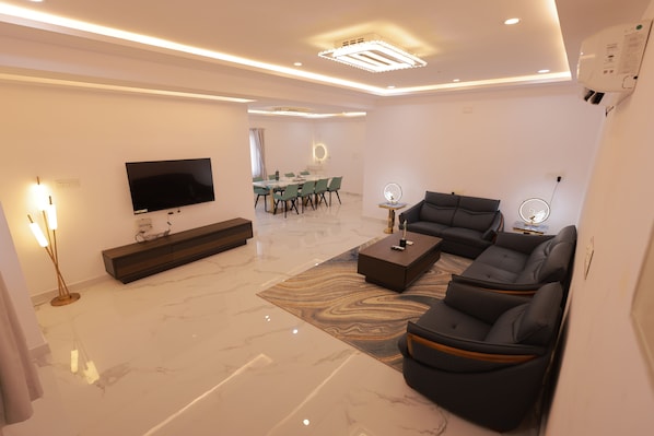 Uma sala moderna com televisão de tela plana, sofá seccional, mesa de centro e área de jantar com mesa e cadeiras.