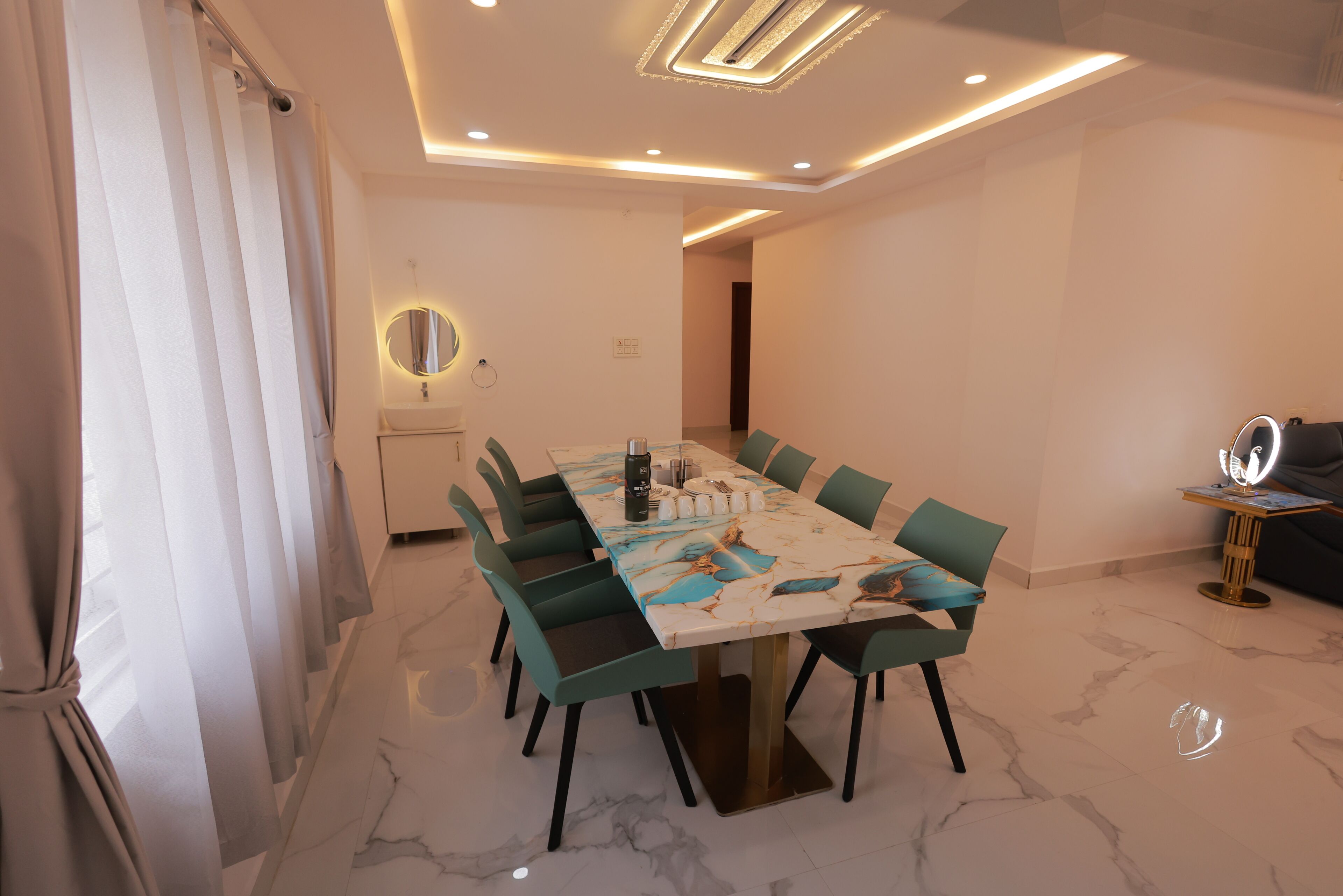 Un comedor moderno con suelo de mármol, un espejo redondo y una mesa preparada para seis comensales.