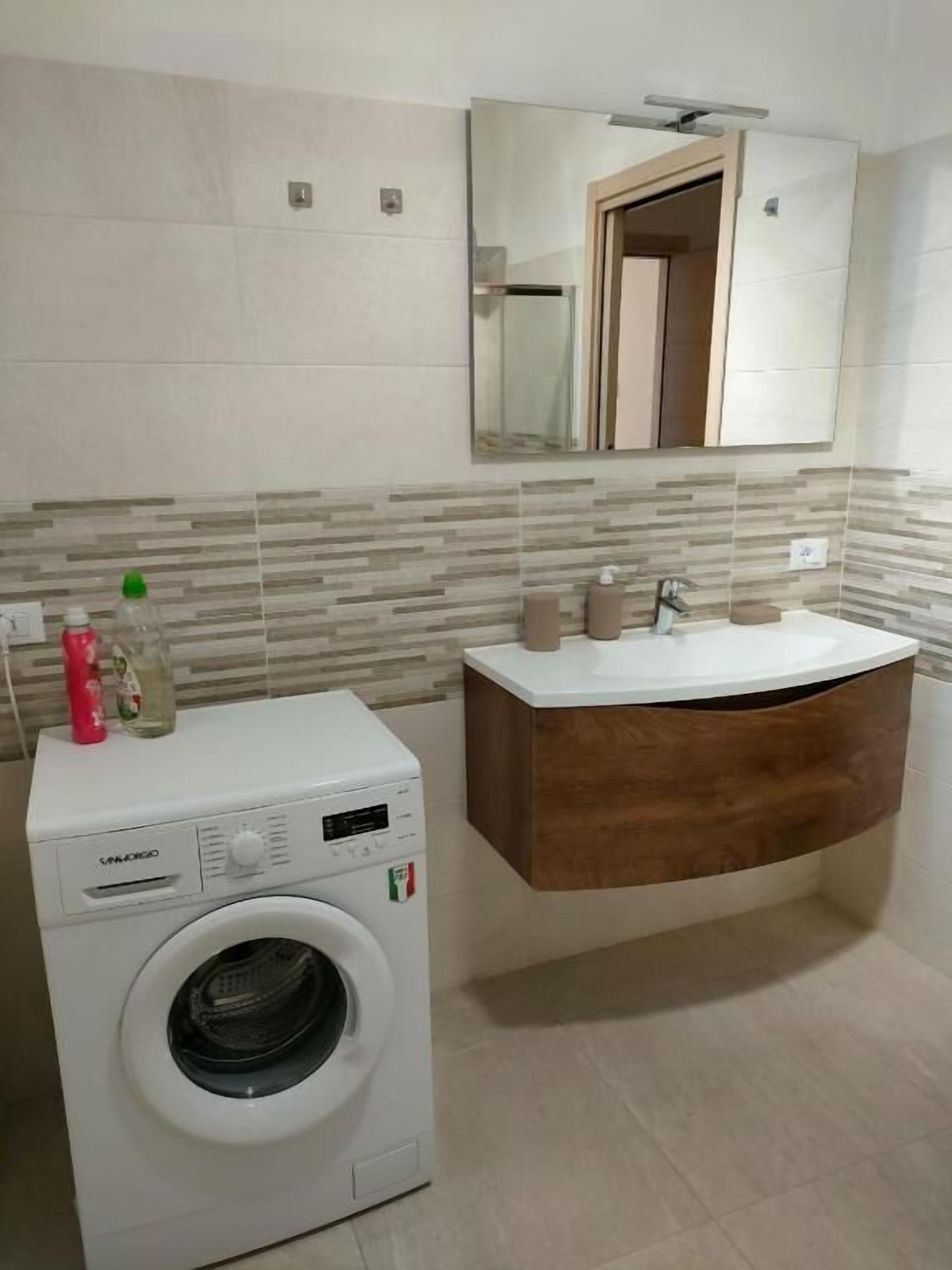 Une salle de bain moderne dotée d’un lave-linge intégré, d’un meuble-lavabo en bois et d’un grand miroir.