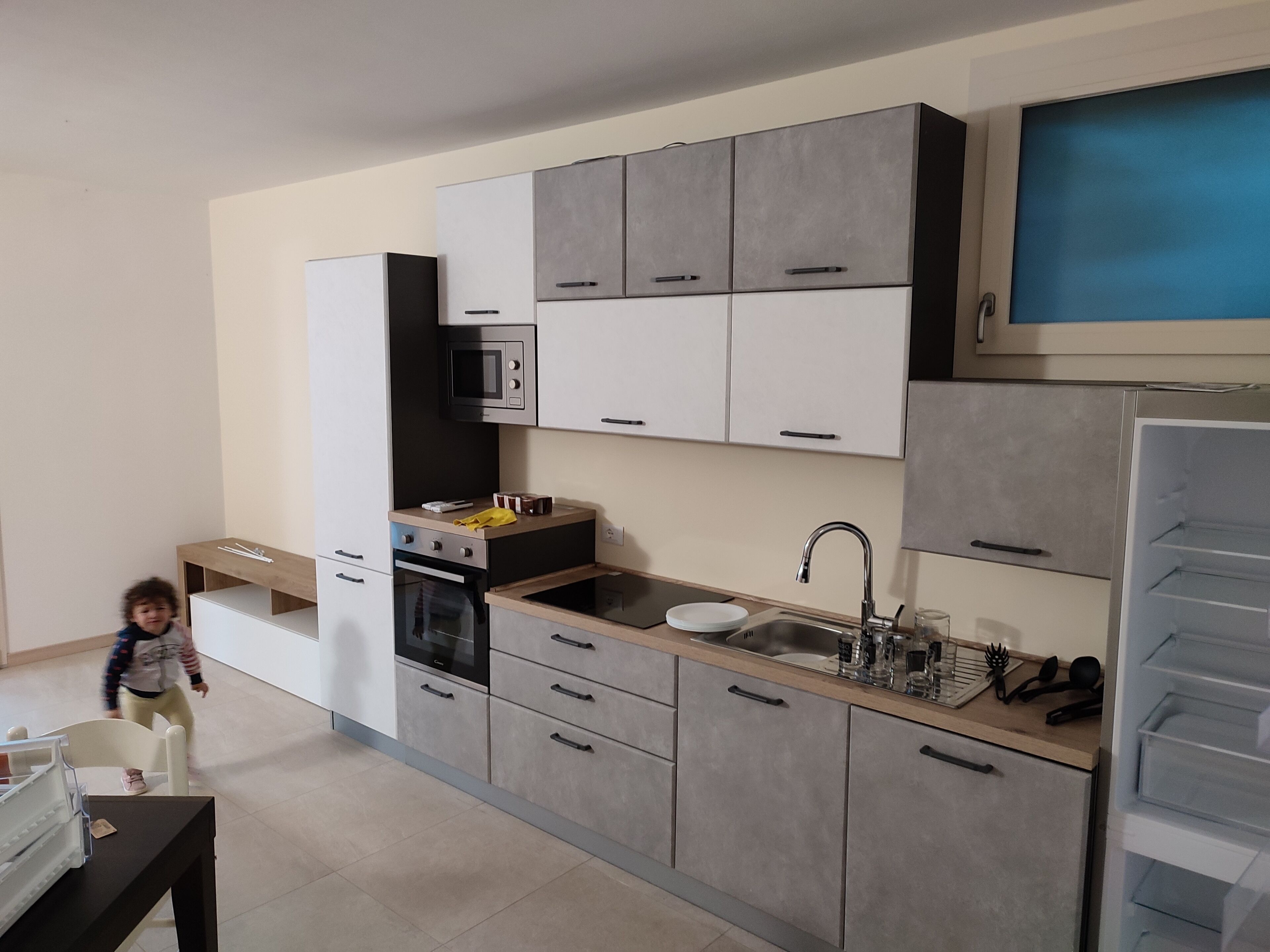 A modern kitchen with grey cabinets, a microwave, a sink, and a built-in oven.