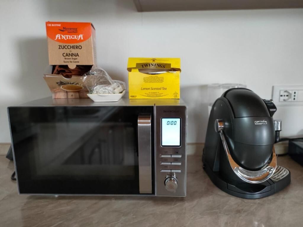 A microwave with a digital display, a coffee maker, and boxes of food items on a countertop.