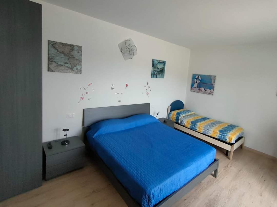 Une chambre à coucher avec un grand lit, un plus petit lit, une table de chevet et un mur décoré d’œuvres d’art.