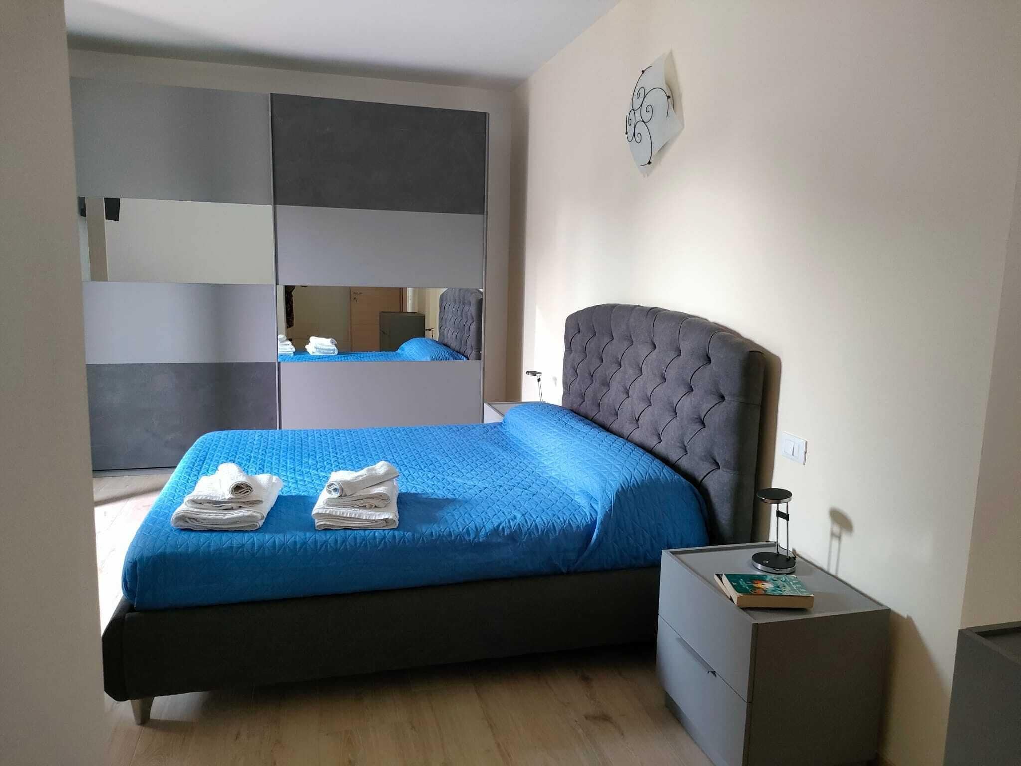 A bedroom with a bed, a nightstand, a mirror, and a wall-mounted light fixture.