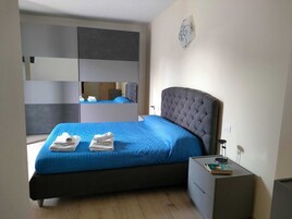 Un dormitorio con cama, mesita de noche, espejo y lámpara de pared.