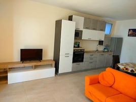 Una cocina moderna con electrodomésticos integrados, un comedor con banco y un sofá naranja.