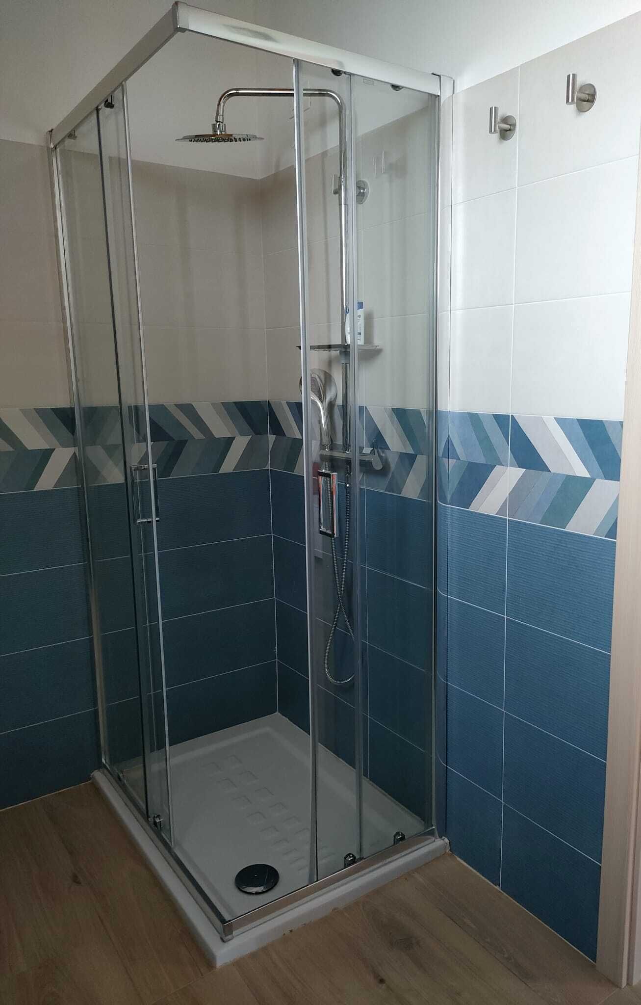 A glass-enclosed shower stall with a handheld showerhead and a handheld faucet.