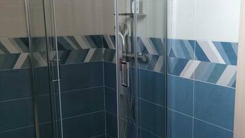 A glass-enclosed shower stall with a handheld showerhead and a handheld faucet.