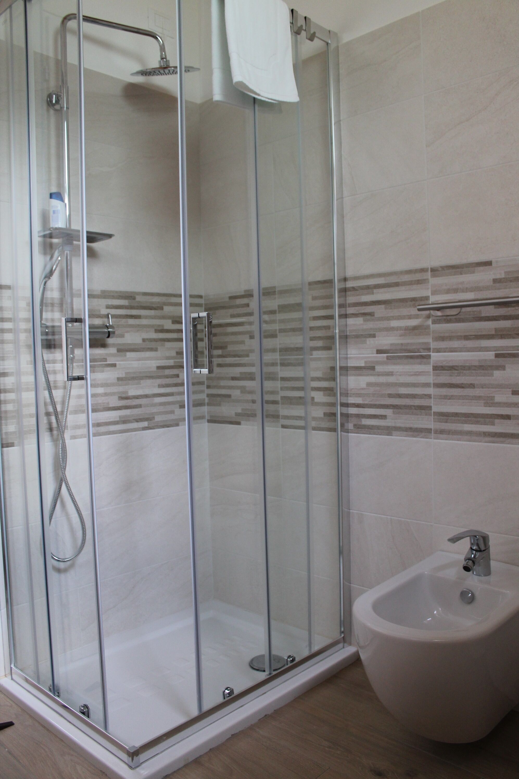 A glass-enclosed shower with a handheld showerhead and a wall-mounted faucet.