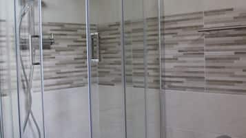 A glass-enclosed shower with a handheld showerhead and a wall-mounted faucet.