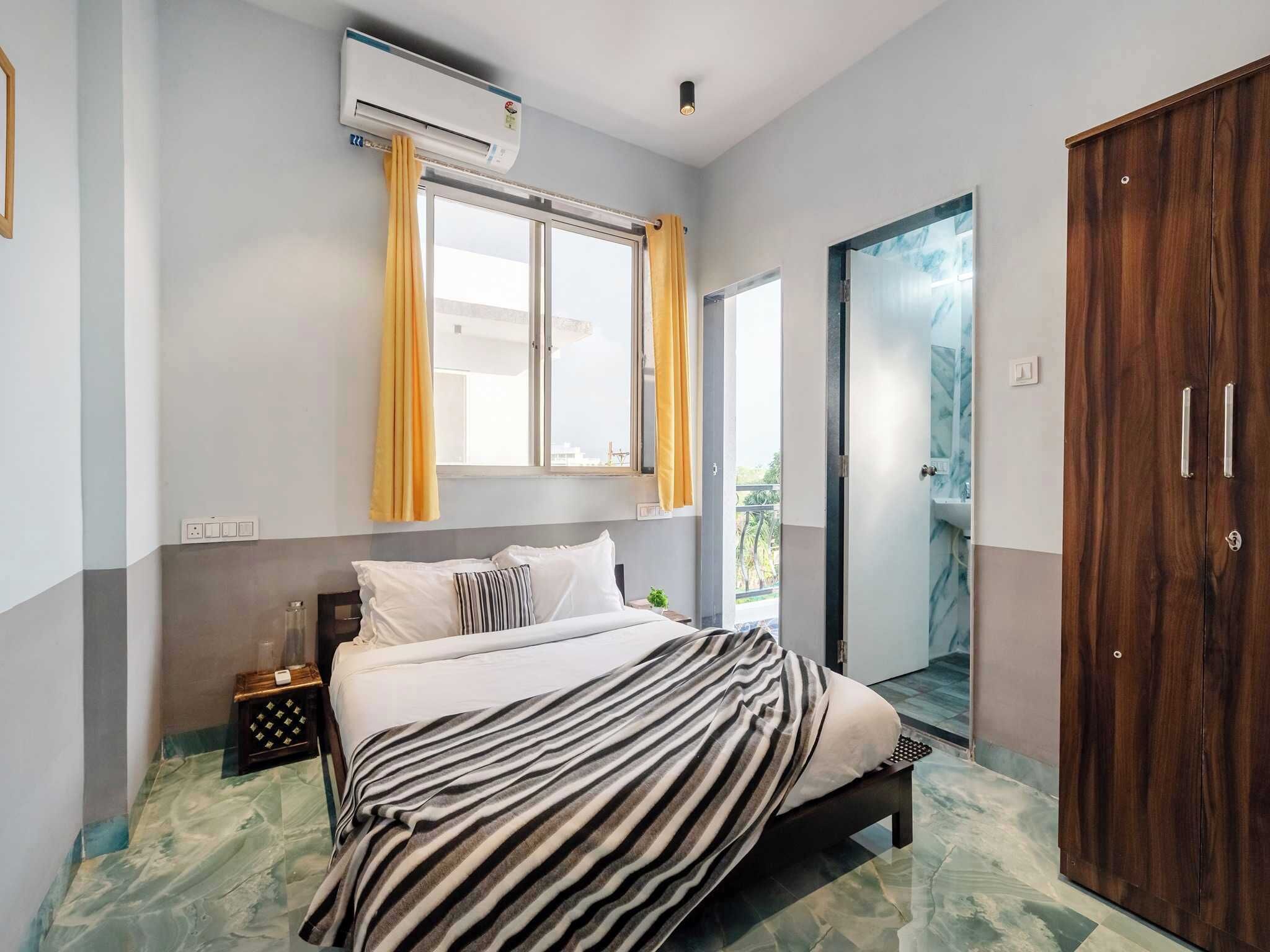 A bedroom with a bed, a wardrobe, a window with curtains, and an air conditioning unit.